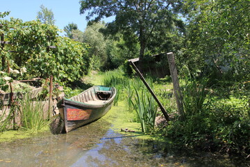 wooden boat resting on muddy ground in a sun-dappled garden