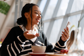 Happy beautiful African American woman having video call on smartphone gesturing