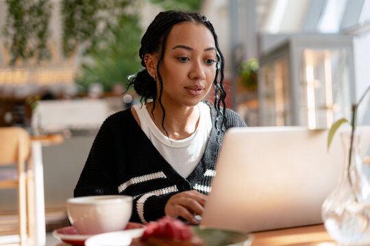 Serious African American woman with piercing remotely working on laptop in cafe, checking mail