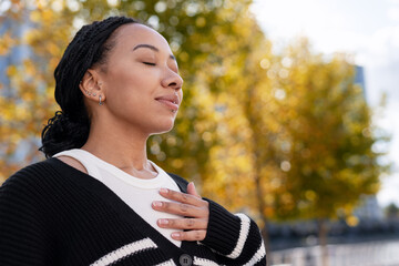 Young beautiful African American woman meditating outdoors feeling peaceful