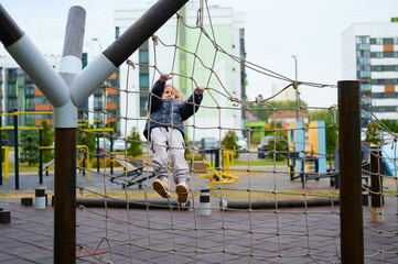 child climbing playground rope net challenges physical abilities and encourages active outdoor adventure. modern urban play area background promotes healthy fitness lifestyle for children