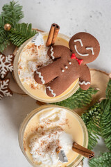 A gingerbread man is sitting on top of a glass of milk with cinnamon sticks