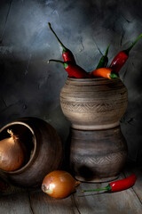 Yellow onion, chili pepper and ceramic pots on a wooden table