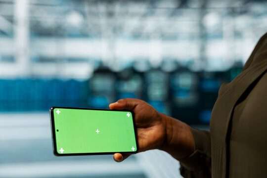 Close up of data center technician checking rigs performance data on chroma key smartphone. Server farm worker using isolated screen mobile phone to look at system alerts, monitoring equipment