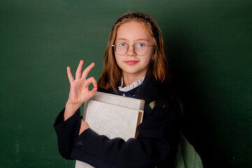 Naklejka premium Back to school. Child holding books on blackboard. School girl. School child. Portrait of elementary pupil. Happy schoolgirl. Schoolkid or preschooler.