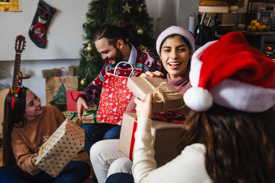 Latin friends exchanging gifts and sitting near Christmas tree at home in Mexico Latin America. Hispanic people at holidays