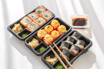 Assorted sushi rolls in plastic delivery boxes with soy sauce, ginger, and wasabi concept of Japanese cuisine, takeaway food, and convenient modern dining