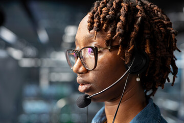 Close up of female technician on industrial platform speaks in headset mic, overseeing maintenance on AI server rigs below. Admin coordinates machine learning system operations.