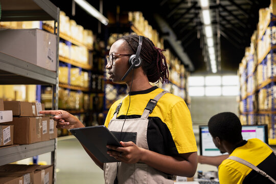 Call center female worker answers help line call in a logistics warehouse, updating clients on orders and resolving cargo mix ups. Managing inventory control in order to fix barcode issues.