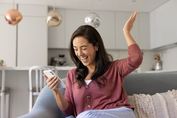 Cheerful excited Hispanic smartphone user woman celebrating online win