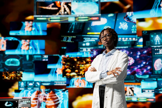Portrait of healthcare specialist reviewing CT scans, MRI data, and lab analytics displayed on videowall. Scientist in medical research lab visualizing health data on futuristic panels