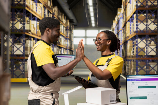 African american team sharing a joyful high five gesture in busy warehouse environment, being proud and pleased with their express delivery success. Finishing tasks on time to ensure workflow. - Powered by Adobe
