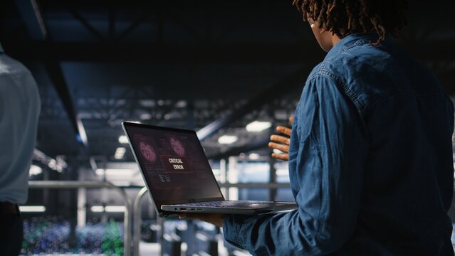 Data center software developer panicking after receiving critical error popup on laptop display. African american woman in server hub alerted by bugs causing low hardware performance, - Powered by Adobe