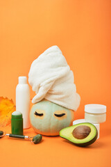 Avocado-based cosmetics concept, pumpkin and various cosmetic containers on orange background, autumn beauty care