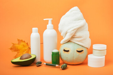 Avocado-based cosmetics concept, pumpkin and various cosmetic containers on orange background, autumn beauty care