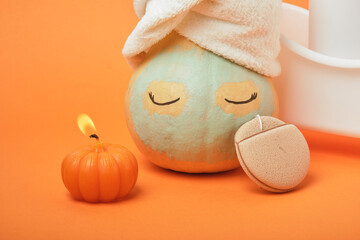 Pumpkins and bottles of cosmetic products on bright orange background, candles and reusable pad, autumn self care