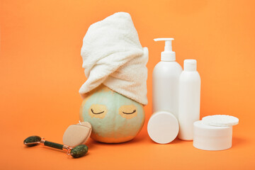 Pumpkin with face and towel in clay mask on orange background, natural cosmetics concept, autumn skincare routine