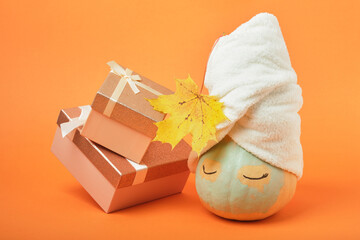 A pumpkin smeared with clay with a towel on top and gift boxes on an orange background, the time for holiday gifts and sales concept