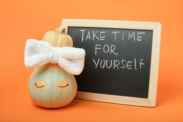 A cute pumpkin from a spa salon and a chalkboard with the inscription "take time for yourself" on an orange background