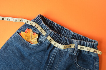Measuring tape and jeans on an orange background, the concept of fighting excess weight in the autumn period