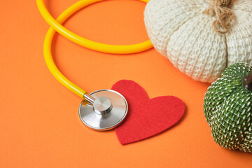 Stethoscope, pumpkin decoration, and heart on an orange background, exacerbation of heart disease in autumn