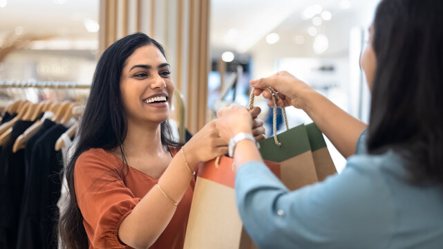 Cheerful Indian customer taking shopping bags with clothes from associate