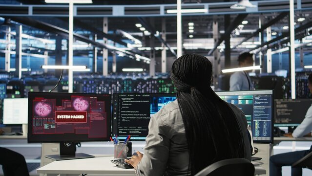 Server farm IT expert responds to security breach alert displayed on computer monitor, working to secure hardware. Data center employee attempts to protect equipment during cyberattack, camera A