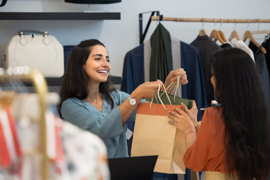 Happy Latin fashion outlet cashier giving shopping bags to customer - Powered by Adobe