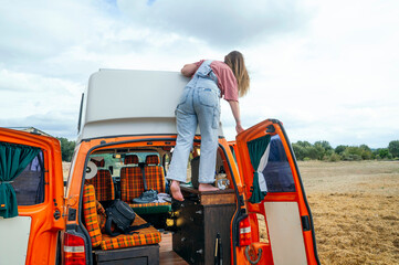 Woman climbing barefoot onto the roof of an orange camper van to clean or check something