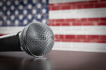 Microphone Resting on a Table with the American Flag Painted On A Brick Wall Behind.