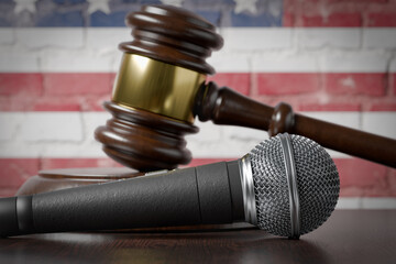 Microphone and Gavel Resting on a Table with the American Flag Painted On A Brick Wall Behind.