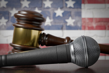Microphone and Gavel Resting on a Table with the American Flag Painted On A Brick Wall Behind.