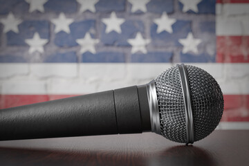 Microphone Resting on a Table with the American Flag Painted On A Brick Wall Behind.