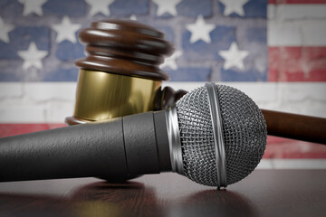 Microphone and Gavel Resting on a Table with the American Flag Painted On A Brick Wall Behind.