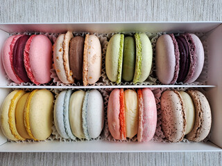 Multi-colored macaroons in a white cardboard box standing on a light gray table. Closeup. Top down view. Shoot on phone camera