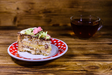 Cup of tea and plate with slice of Kiev cake with cream, nuts and meringue on a wooden table
