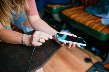 Woman laughing while plugging a charging cable into her smartphone inside a camper van.