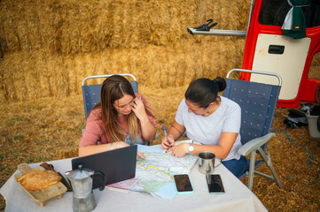 Women planning route with map, notebook, and laptop on table.