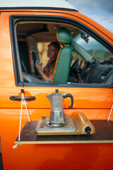Coffee pot on portable stove attached to orange camper van door.