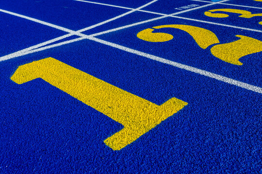Close up photo of outdoor running track lane yellow number one, 1, on a new blue track with white lane lines.