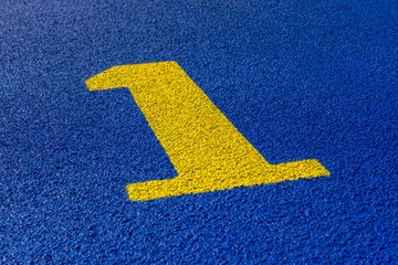 Close up photo of outdoor running track lane yellow number one, 1, on a new blue track with white lane lines.