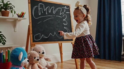 Little blonde girl drawing enthusiastically on chalkboard in cozy room setting with toy bears around. concept of childhood creativity, playful learning, imaginative playtime. - Powered by Adobe