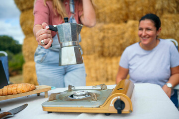 Woman holding coffee pot near portable stove while another woman smiles outdoors.