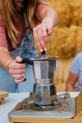 Close-up of woman’s hands preparing coffee with moka pot on portable stove.