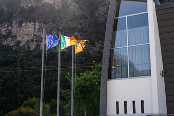 Flags of the European Union, Italy and region of Veneto in front of the Cemetery of the Vajont victims in Longarone, Italy