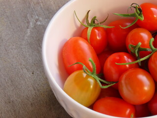 Closeup of bowl of small red tomatoes on wooden surface. Tomatoes in a bowl.