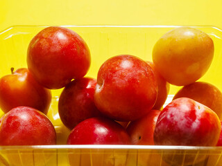Fresh pure nectarine with glossy skin in a plastic basket on sunny yellow background. Agriculture product ready to eat and for sale. Food chain supply. Clean ripe organic product carefully selected.