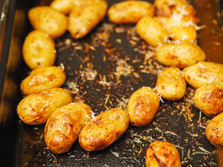 Cooked full uncut potatoes on a dark metal tray with herbs. Fine dinner side dish ready to be served. Home cooking concept.