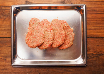 Lamb uncooked steak coated in Arabic Harissa style herbs and spices on stainless metal tray on wooden table. Red minced meat. Fine butcher style burgers ready for cooking.