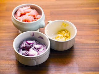 Three white cups wit diced chicken fillets, garlic and onions on wooden table. Cooking dinner concept. Proper preparation.